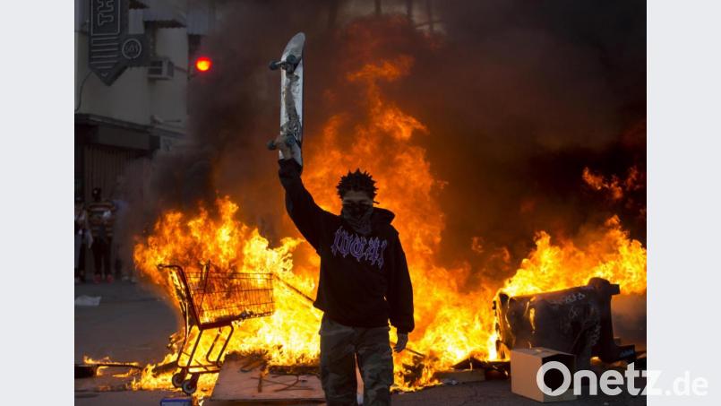 Ein Demonstrant hält in Los Angeles ein Skateboard in die Höhe, während hinter ihm ein Einkaufswagen auf der Straße brennt. Bild: Ringo H.W. Chiu/dpa