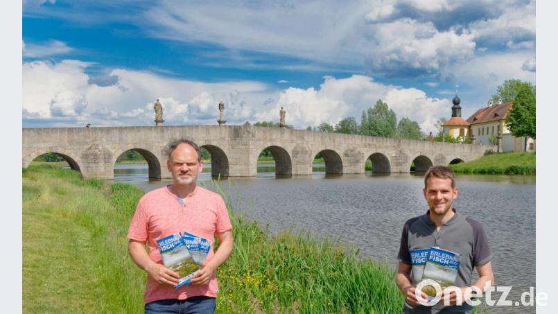 Vor der Kulisse des historischen Fischhofs in Tirschenreuth präsentieren der Vorsitzende der Arge Fisch im Landkreis Tirschenreuth, Thomas Beer (links) und Fabiab Polster vom Landratsamt die Broschüre zu den Erlebniswochen Fisch 20/21. Bild: tr