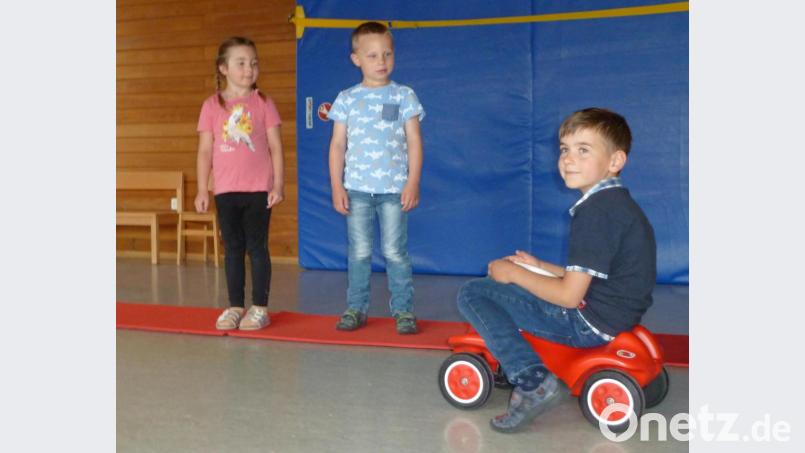 Bevor es zum Schulwegtraining mit den Polizeibeamten ins Freie ging, wurde das Überqueren der Straße in der Turnhalle des Kindergartens St. Marien geübt. Die beiden Vorschulkinder gingen dazu nahe am Haus (blaue Matte) entlang und blieben an der Bordsteinkante (rote Matte) stehen, um zu schauen, ob sich ein Auto (Junge mit Bobby-Car) nähert Bild: Portner