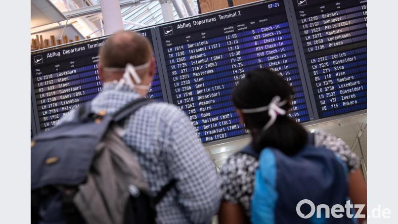Reisende mit Mundschutz schauen auf eine Anzeigetafel am Münchner Flughafen, auf der zahlreiche internationale Flugziele gelistet sind. Bild: Matthias Balk/dpa