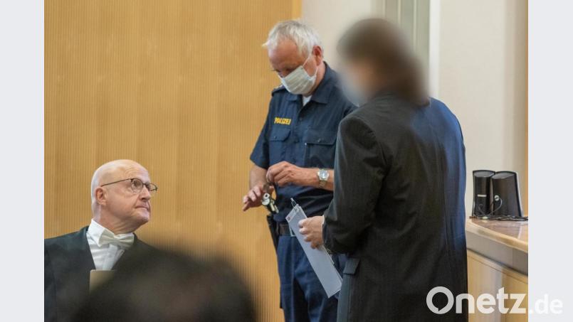 Der Angeklagte (rechts) steht im Verhandlungssaal des Landgerichts neben einem Polizisten und seinem Verteidiger Michael Haizmann (links). Acht Jahre nach dem gewaltsamen Tod von Maria Baumer hat vor dem Landgericht Regensburg der Mordprozess gegen ihren Verlobten begonnen. Nach Überzeugung der Staatsanwaltschaft hat der Mann sein Opfer mit Medikamenten getötet und die Leiche in einem Wald vergraben. Der Verlobte hatte Maria Baumer im Mai 2012 als vermisst gemeldet. Bild: Armin Weigel/dpa