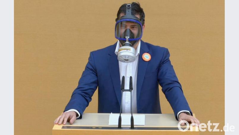 Der Screenshot aus einem Video zeigt den AfD-Abgeordneten Stefan Löw mit einer Gasmaske am Rednerpult im Bayerischen Landtag. Bild: Bayerischer Landtag/dpa