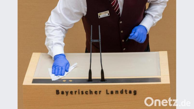 Ein Mitarbeiter des Landtags desinfiziert während der Plenarsitzung des bayerischen Landtags das Rednerpult. Bild:  Peter Kneffel/dpa