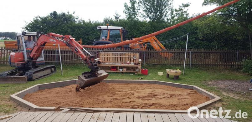 Den von einem Pressather Unternehmen gestifteten Sand füllen die Mitarbeiter des Trabitzer Gemeindebauhofs in den Sandkasten des Kindergartens. Bild: bjp