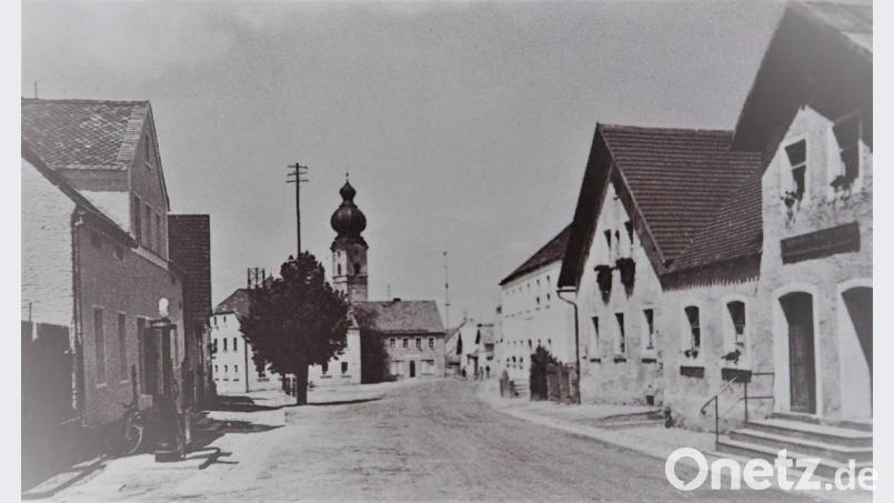 Die Aufnahme von 1937 zeigt die Kirche nach dem Brand mit dem neuen Turm und am Tillyplatz auf der linken Seite die Tankstelle und das Geschäftshaus Müller (Waldmüller) und rechts die Anwesen Lang (Alisn), Wild (Gougl) und Meckl (Pöiterlsimmer). Bild: exb