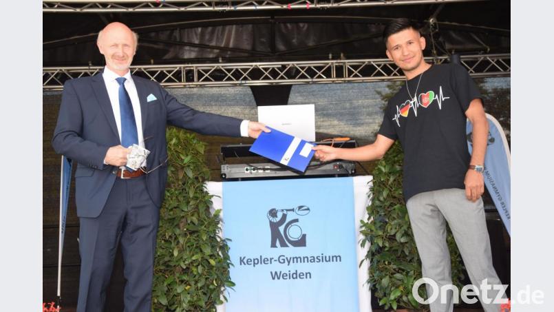 Nezamuddin Haydari (rechts) darf von stellvertretendem Schulleiter Johannes Wagner das Abiturzeugnis entgegennehmen. Innerhalb von fünf Jahren hat der 21-jährige Afghane nicht nur Lesen und Schreiben gelernt, sondern auch die Abiprüfung am Kepler-Gymnasium in Weiden erfolgreich gemeistert. Auf seinem T-Shirt zeigt er: In ihm schlagen ein deutsches und ein afghanisches Herz. Bild: fz