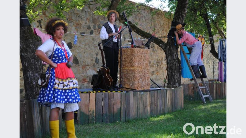 Die Bühne im Schloßgarten der Friedrichsburg. Die Kuh Rosmarie (Mona Fischer) stänkert am Bauern (Johannes Aichinger, rechts) herum. Klangtechnisch untermalt von Martin Kubetz (Mitte). Bild: gge