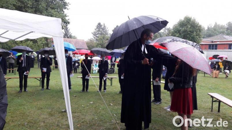 Unter dem Regenschirm segnet Pfarrer Uwe Markert die Jugendlichen ein. Bild: exb