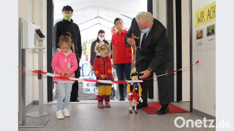 Zweiter Bürgermeister Peter Gold durchschneidet zusammen mit seiner Marionette Pinocchio und den ersten Weltentdeckerinnen das symbolische Band zur Eröffnung des BRK-Kinderhauses. Bild: Sven Lehner/exb