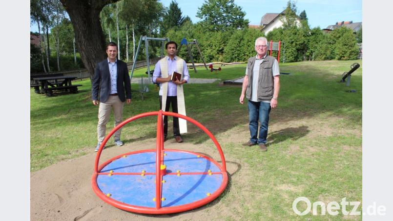 Bürgermeister Wolfgang Söllner, Pfarrer Pater Anish George und „Bauleiter“ Hubert Becher bei der Einweihung der neuen Spielgeräte. Hier das neue Drehkreuz. Bild: soj