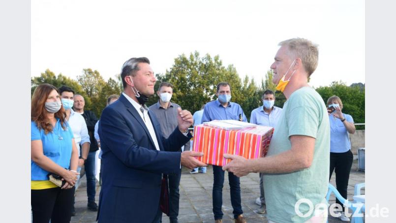 Produktionsleiter Thomas Blieninger (rechts) überreicht unter Einhaltung des Abstandes Bürgermeister Rainer Rewitzer ein verspätetes Geburtstagsgeschenk. Darüber freut sich besonders dessen Ehefrau Corinnna (links). Bild: bey
