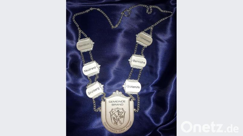 Mit einer neuen Amtskette dankte der neue Altbürgermeister der Gemeinde Brand für die Auszeichnung. Neben dem großen Schild mit Wappen und Hinweis auf Max Reger sind alle sechs zur Gemeinde gehörenden Ortsteile benannt. Bild: ld