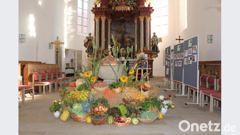 Der Erntegaben sind am historischen Taufstein der Dreieinigkeitskirche und auf einem Leiterwagen dekoriert. Im Hintergrund sind Stellwände mit Fotos zu sehen: „Vom Korn zum Brot“ – oder besser „Ein Brot erzählt aus seinem Leben“. Bild: rpp
