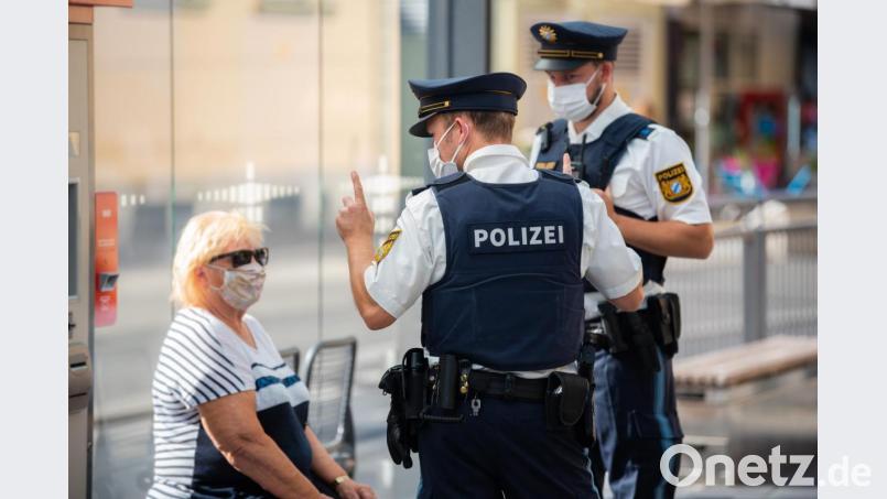 Zwei Polizisten nehmen an einer Tram-Haltestelle in Würzburg von einer Frau nach einem Verstoß gegen die Maskenpflicht im öffentlichen Nahverkehr die Personalien auf. Foto: Nicolas Armer/dpa Bild: Nicolas Armer