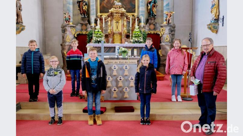 An den Stufen zum Altarraum der Pfarrkirche St. Luzia in Schlammersdorf nimmt Andreas Steinl, Co-Vorsitzender der Kinderkrebshilfe Oberpfalz Nord, die 870-Euro-Spende der sieben Erstkommunionkinder und ihrer Eltern entgegen. Bild: do