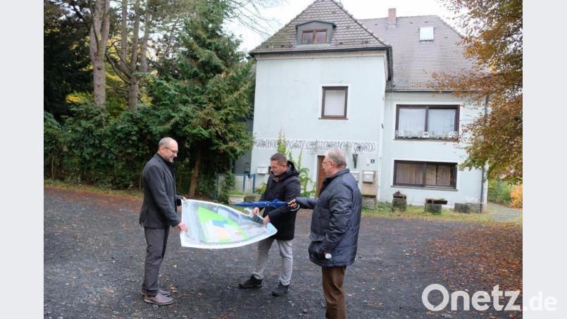 Bürgermeister Marcus Gradl (Mitte), zweiter Bürgermeister Karl Lorenz (links) und dritter Bürgermeister Udo Müller (rechts) freuen sich über den Erwerb des Bundscherer-Anwesens (im Hintergrund) und denken mit Blick auf den Lageplan über die vielversprechenden Nutzungsmöglichkeiten nach. Bild: do