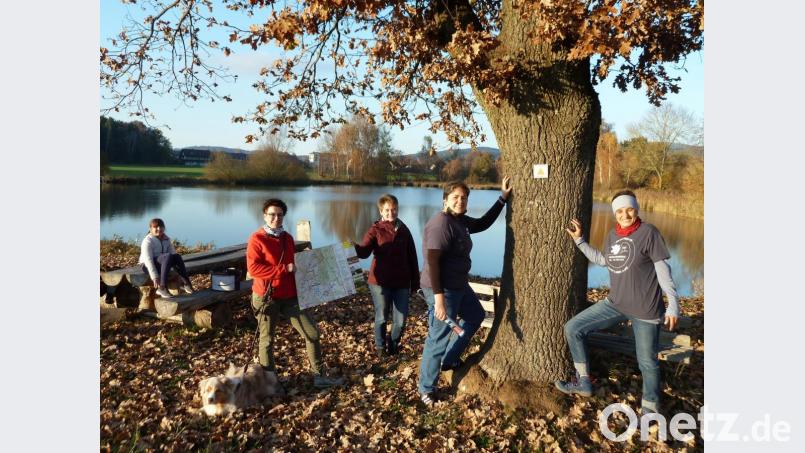 Der Weiher bei Muschenried ist auch im Herbst ein Naturjuwel. Anja Ried (rechts) und Johanna Bösl kleben die Markierung für den „W 3“-Weg an den Baumstamm. Ramona Griebl und Bürgermeisterin Sonja Meier (Mitte) präsentieren die Wanderkarte, und Lucie testet die Sitzbank. Bild: Portner