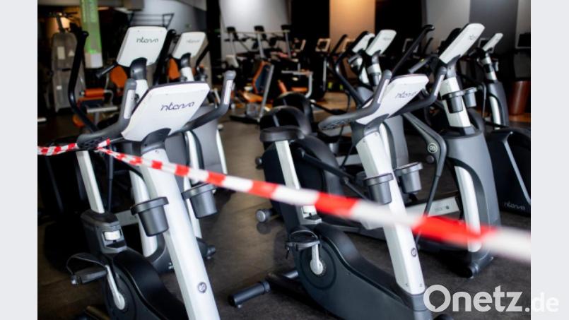 Ein rot-weißes Flatterband ist an Fahrradtrainern befestigt, die in einem Fitnessstudio stehen. Unter bestimmten Einschränkungen dürfen Studios bald wieder öffnen. Bild: Hauke-Christian Dittrich/dpa
