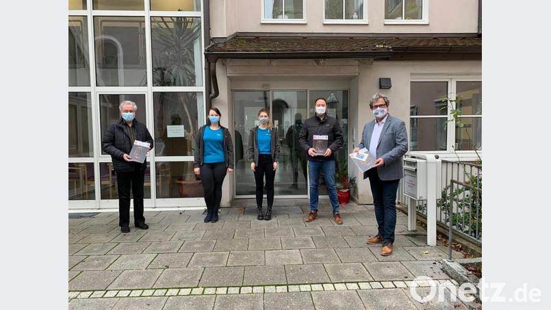 Bürgermeister Bernhard Stangl, Christian Fuchs vom Caritas-Pflegeheim (von rechts) und Pfarrer Edmund Prechtl (von links) halten den Jahreskalender 2021 in den Händen, den Katharina Dörner und Lee-Ann Kagerer im Namen der Festdamen der Feuerwehr überreichen. Bild: jma