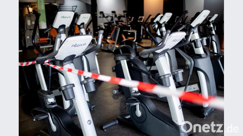 Ein rot-weißes Flatterband ist an Fahrradtrainern befestigt, die in einem Fitnessstudio stehen. Bild: Hauke-Christian Dittrich/dpa