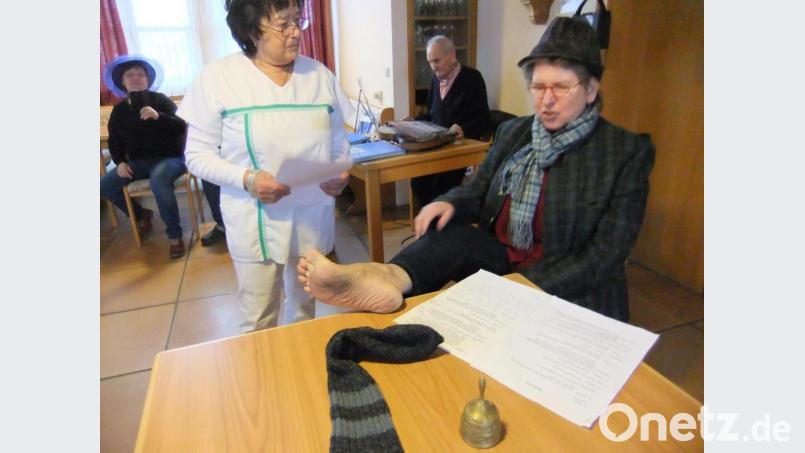 Die Jubilarin Annemarie Neidl (rechts mit Hut) als Sketch-Laienspielerin und Patientin beim Arzt mit dem Fuß auf dem Tisch des Doktors. Die Lacher hat sie so natürlich stets auf ihrer Seite. Archivbild: gm