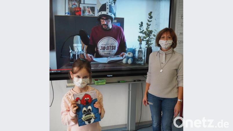 Stolz präsentiert Jessica (links) ihr Lieblingsbuch. Der Autor ist ihr Vater Andreas Fachtan (Mitte, im Display). Für den bundesweiten Vorlesetag schickte er Klassenleiterin Sonja Brunner-Rosner (rechts) eine Videobotschaft für die Klasse 2b , in der er aus seinem Buch &quot;Großes blaues Bärenwort&quot; vorlas. Bild: jpl