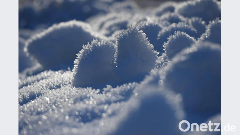 Eiskristalle sind auf einer Wiese im Schnee zu sehen. Bild: Angelika Warmuth/dpa