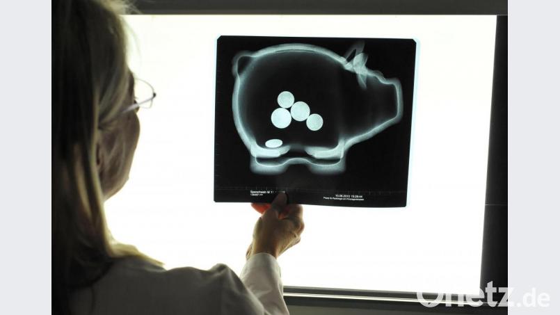 Eine Radiologin hält eine Röntenaufnahme eines Sparschweins gegen einen Leuchtkasten: Der Amberg-Sulzbacher Landrat Richard Reisinger sieht das derzeitige Finanzierungssystem der Krankenhäuser und daraus resultierende Klinik-Schließungen mit Sorge. Bild: Peter Kneffel/dpa
