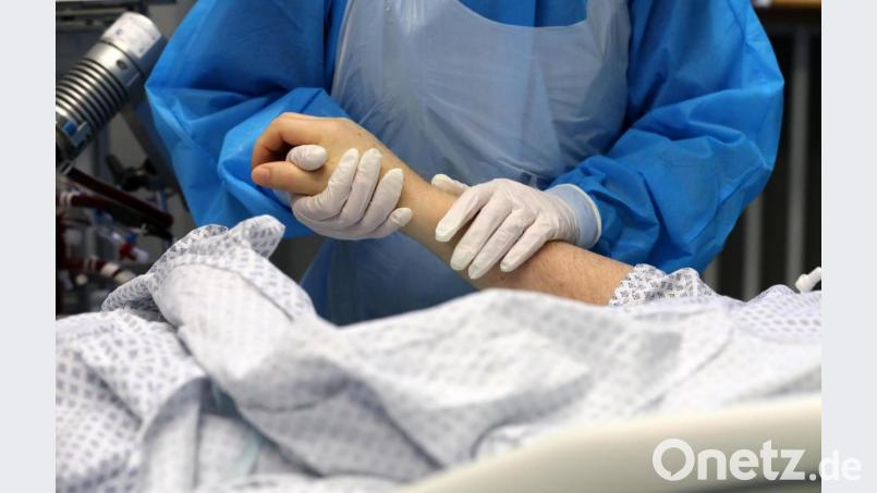 Im Infektionszimmer für Covid-19-Patienten hält die Mitarbeiterin einer Intensivstation die Hand eines Patienten. Bild: Bernd Wüstneck/dpa