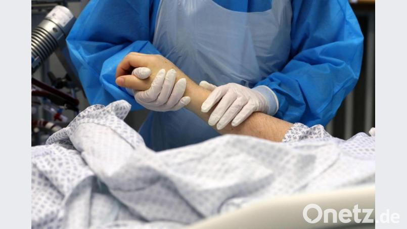 Im Infektionszimmer für Covid-19-Patienten hält die Mitarbeiterin einer Intensivstation die Hand eines Patienten. Foto: Bernd Wüstneck/dpa-Zentralbild/dpa/Archivbild Bild: Bernd Wüstneck