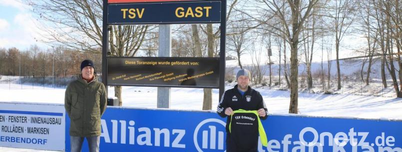 Einen Teil der neuen Trainingsanzüge hält Jugendleiter Marco Manze (rechts) in Händen. Wolfgang Hoffmann (links) von der Nachwuchsförderung überreichte ihm 60 Stück der Anzüge. Im Hintergrund ist die neue elektronische Anzeigetafel zu sehen. Bild: njn