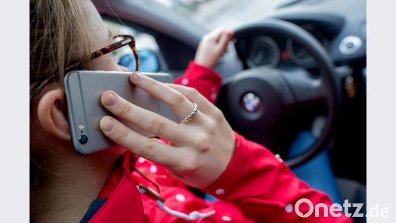 Eine junge Frau telefoniert am Steuer ihres Wagens (Symbolbild): In Amberg hat das eine Frau sogar zweimal hintereinander getan – und wurde beide Male von der Polizei erwischt. Bild: Hauke-Christian Dittrich/dpa