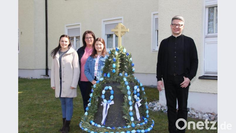 Als Familienaktion gestaltet sich das Schmücken der alten Glocke im Pfarrgarten von St. Konrad für Manuela Weigl (hinten) und ihre beiden Töchter Leonie und Johanna (vorne, von links). Pfarrer Michael Jakob freut sich wie die Passanten an der geschmückten Osterglocke – heuer in den Bayernfarben. Bild: ads