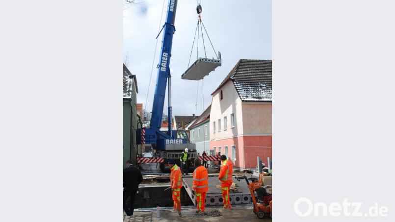 Ein Autokran hievt das dritte Teil der neuen Brücke über den Floßbach auf das Widerlager. Bild: tss