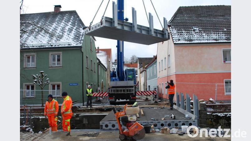 Ein Autokran hievt das dritte Teil der neuen Brücke über den Floßbach auf das Widerlager. Bild: tss