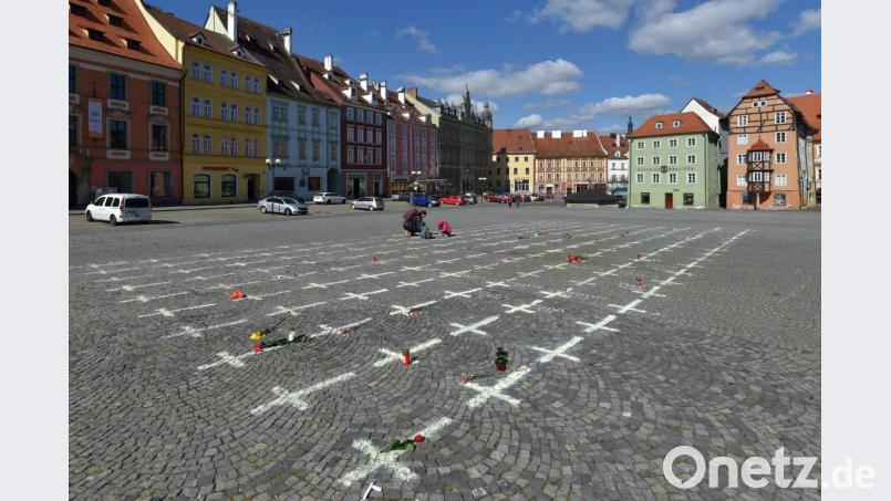 Kerzen und Blumen liegen neben weißen Kreuzen, die auf das Pflaster eines Platzes in Eger gemalt wurden. Die Kreuze erinnern an die Opfer der Corona-Pandemie. Bild: Kubeš Slavomír/CTK/dpa