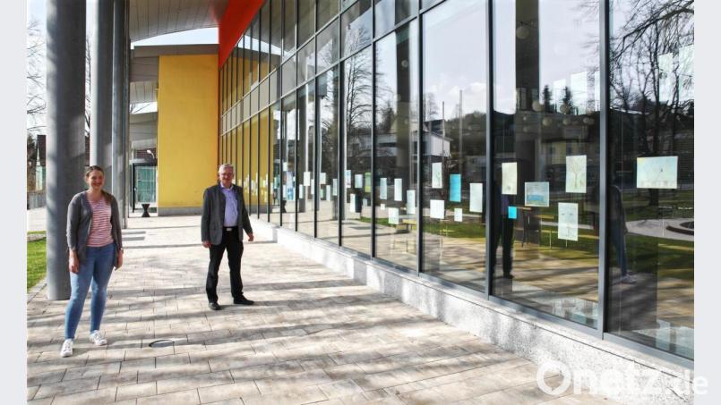 Das Bild zeigt (von links) die Organisatorin des Poesie-Weges und des Rahmenprogramms, Carolin Böckl, und Bürgermeister Johannes Reger vor der Fensterfront der Stadthalle mit den vielen Bildern. Bild: njn