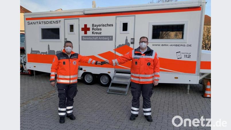 Der bisherige Bereitschaftsleiter Wolfgang Potsch (links) übergibt die Dienststellungsabzeichen an den neuen Bereitschaftsleiter Nicolas Stoffregen (rechts). Im Hintergrund die aktuell als Teststation genutzte Sanitätsstation der Bereitschaft Amberg 1. Bild: Franziska Rubenbauer/exb