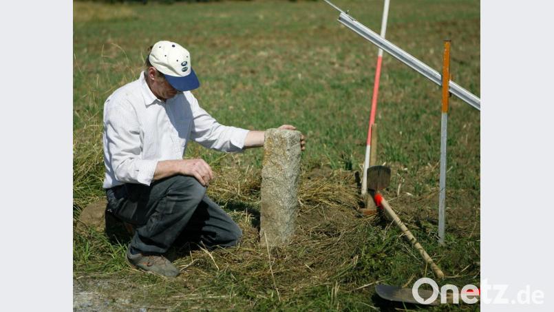 Ein Feldgeschworener hält an einem Feld einen Granit-Grenzstein in der Hand (Symbolbild): Auf Anregung des Vermessungsamts hat es im Bereich von Hirschbach kleinere Gebietsänderungen gegeben. Der Landkreis schrumpft dadurch ein bisschen. Symbolbild: Daniel Karmann/dpa