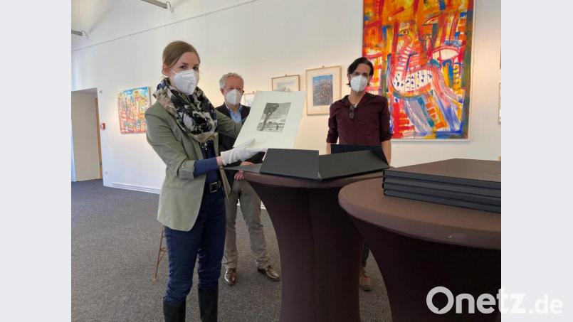 Die erste offizielle Amberger Kunstmappe ist fertig. Ganz vorsichtig nimmt Julia Riß, die Leiterin des Stadtmuseums, Joe Ferstls &quot;Unter schwerem Himmel&quot; heraus. Kulturreferent Fabian Kern (Mitte) und A.K.T.-Vorsitzender Marcus Trepesch freuen sich auf mögliche Käufer. Bild: ass