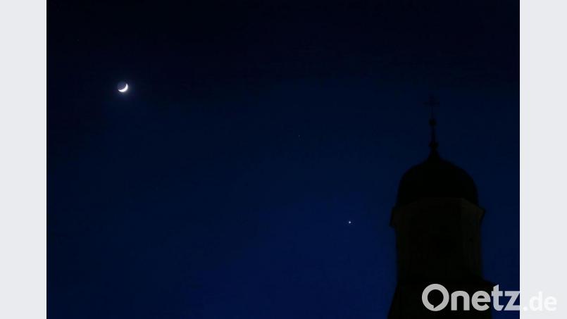 Der zunehmende Mond (links) und der hellleuchtende Planet Venus (rechts) stehen hinter einem Kirchturm am Abendhimmel. Bild: Karl-Josef Hildenbrand/dpa