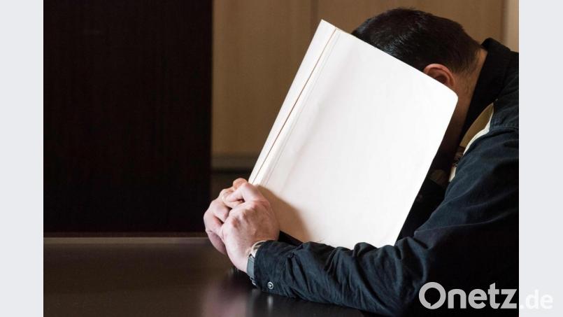 Ein Angeklagter sitzt in einem Gerichtssaal und verdeckt sein Gesicht mit einem Aktenordner. Die Tätowierung auf den Händen wurde aus rechtlichen Gründen gepixelt. Bild: Federico Gambarini/dpa