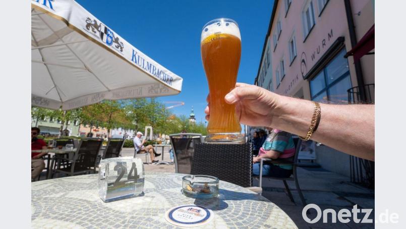 Ein Mann hält ein Glas mit Weißbier im Außenbereich von einer Eisdiele in Tirschenreuth hoch. Bild: Armin Weigel/dpa