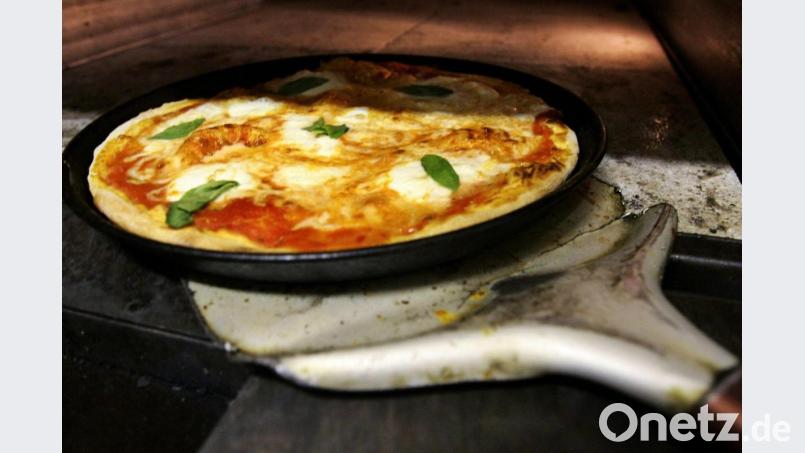 Ein Pizzabäcker holt eine Pizza aus dem Ofen. Symbolbild: Arno Burgi/dpa