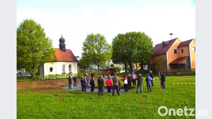 Die Herz Jesu Kapelle links und das Feuerwehrgerätehaus rechts. Der begradigte Der Silberbach plätschert zwischen ihnen durch. Von Teilnehmern aus der Dorfgemeinschaft wurde bemängelt, dass die großen Laubbäume die Sicht auf den Maibaum verdecken würden, der in der Nähe des Bachufers seinen neuen Standort findet. Bild: bkr