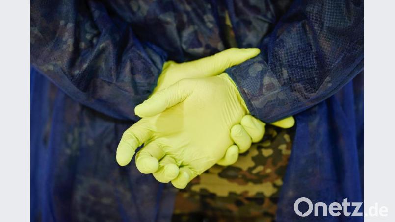 Ein Soldat der Bundeswehr trägt an den auf dem Rücken verschränkten Händen grüne Gummihandschuhe. Im Rahmen des Freiwilligen-Netzwerks «Helfende Hände» organisiert die Bundeswehr schnelle Hilfe in Alten- und Pflegeeinrichtungen. Bild: Uwe Anspach