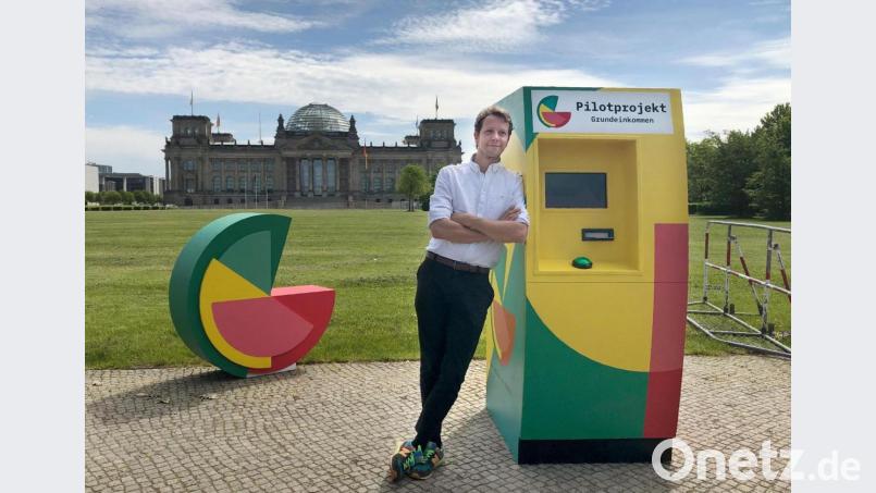 Bedingungsloses Grundeinkommen

Michael Bohmeyer, Initiator des Vereins "Mein Grundeinkommen", steht an einem symbolischen Geldautomaten, im Hintergrund das Reichstagsgebäude. Nach einem langen Auswahlverfahren bekommen 122 Menschen in Deutschland ab jetzt für drei Jahre ein monatliches bedingungsloses Grundeinkommen von 1200 Euro. Symbolbild: Jörg Ratzsch/dpa