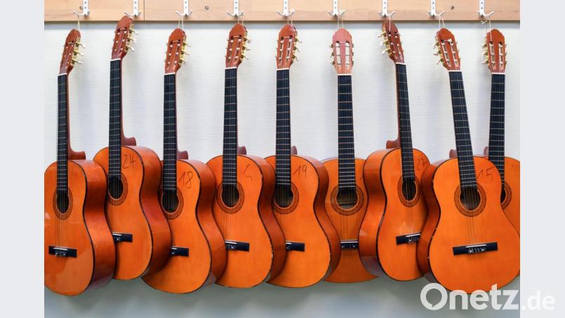 Nummerierte Gitarren für den Musikunterricht hängen an einer Wand. Nach monatelanger Corona-Zwangspause dürfen an den Musikschulen in Bayern seit Montag Gruppen und Ensembles wieder gemeinsam proben. Bild: Patrick Pleul/dpa
