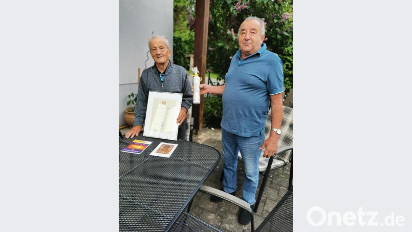Erster Obmann der MMC Schlammersdorf, Emil Gottwald, überreicht die Ehrenurkunde zusammen mit einer Kerze an Alois Püttner (rechts). Bild: hzi