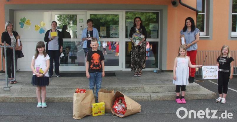 Das von Martina Weiß (hinten, Dritte von links) mitgebrachte Party-Überraschungspaket nahmen vier Grundschüler in Empfang. &quot;20 Jahre GfI Weiden - wir feiern mit&quot;, stand auf dem Plakat (rechts). Zudem im Bild: die Rektorin der Mittelschule, Andrea Schiml, die Vertreterinnen des Betreuungsteams Janine Bartl und Manuela Ponath (von links) und die Rektorin der Grundschule, Inge Dick (rechts). Bild: wro